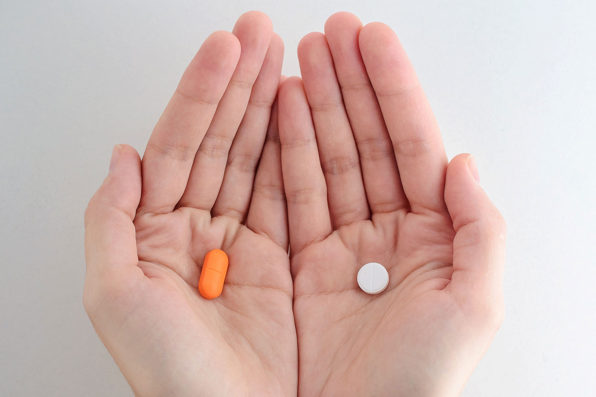 Hands with a different pill in each hand. White and orange